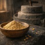 Tradiční kanárské gofio – pražená celozrnná mouka z kukuřice v dřevěné misce na vulkanickém kameni, s historickým kamenným mlýnem v pozadí, symbol potravinové tradice Kanárských ostrovů.